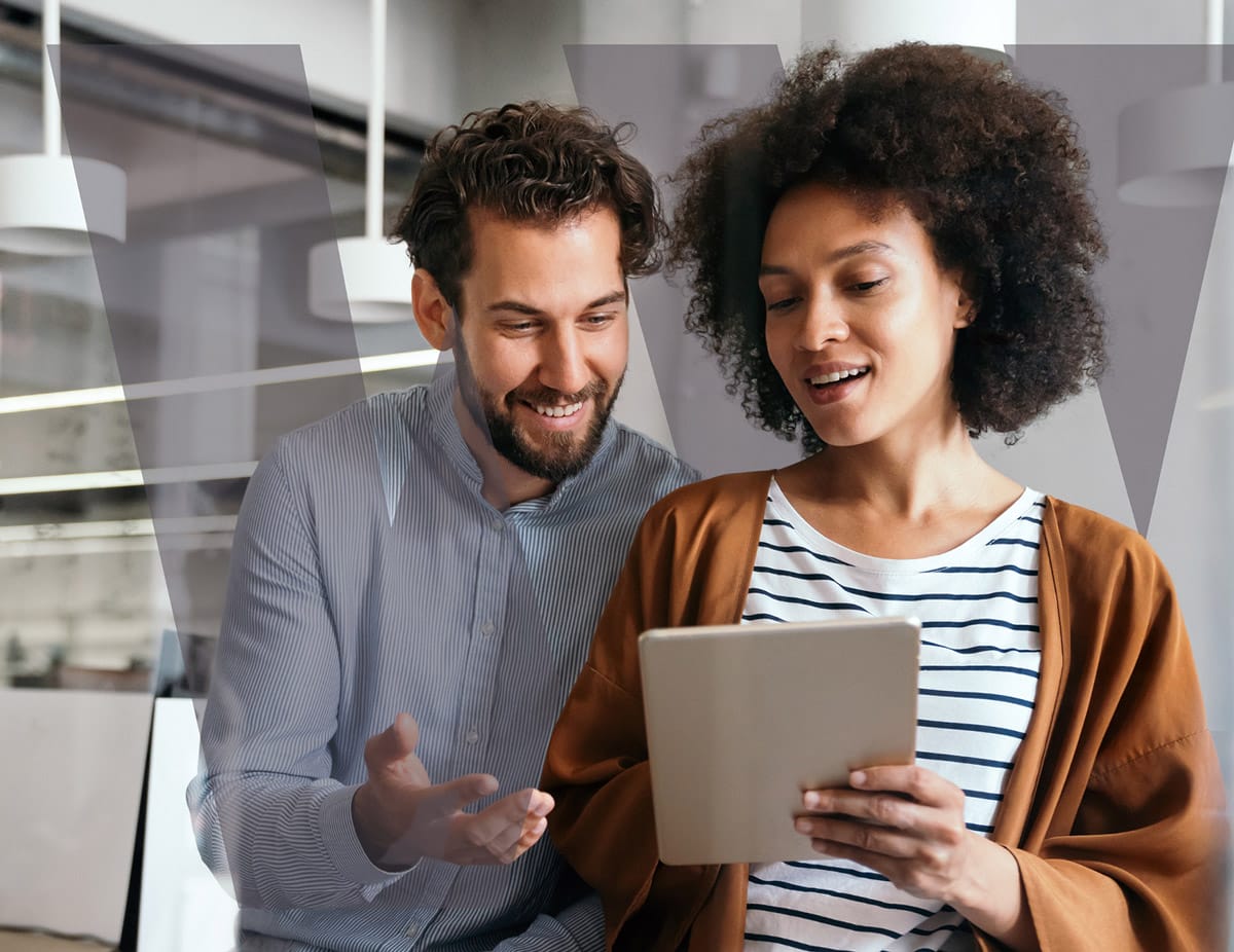 Smiling man and woman collaborating while looking at a tablet in a modern office setting.