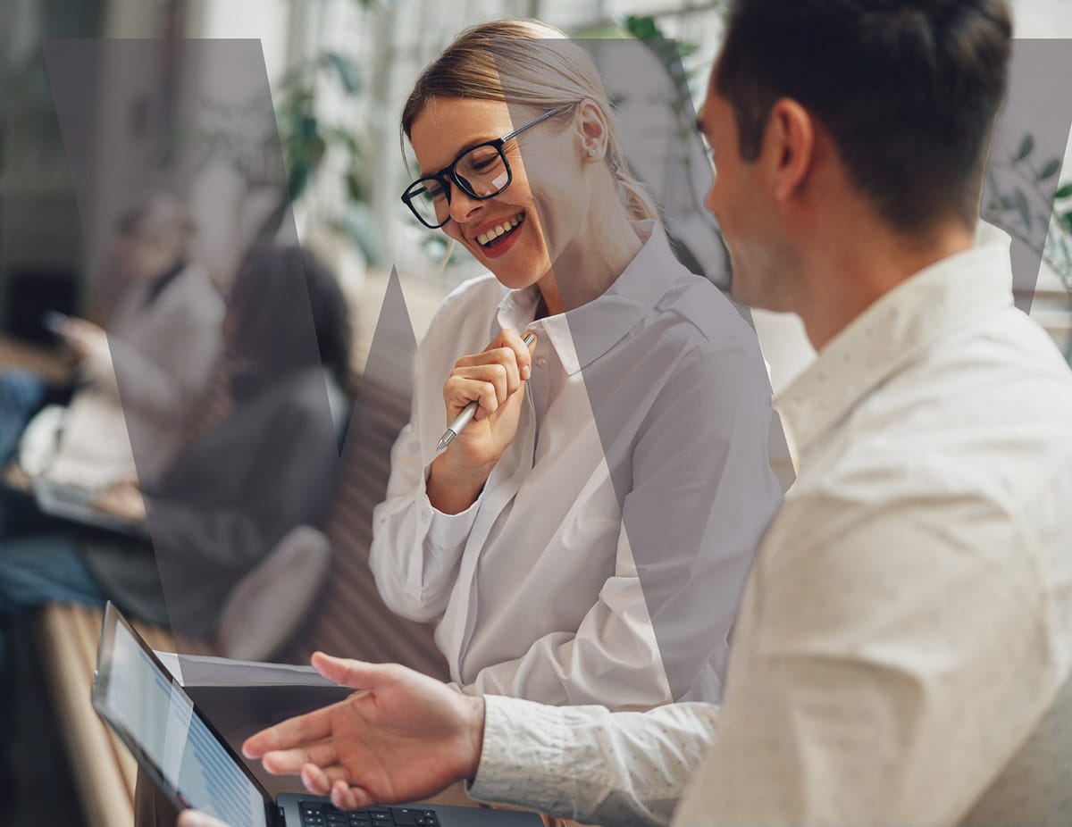 Smiling man and woman collaborating while looking at a tablet in a modern office setting.