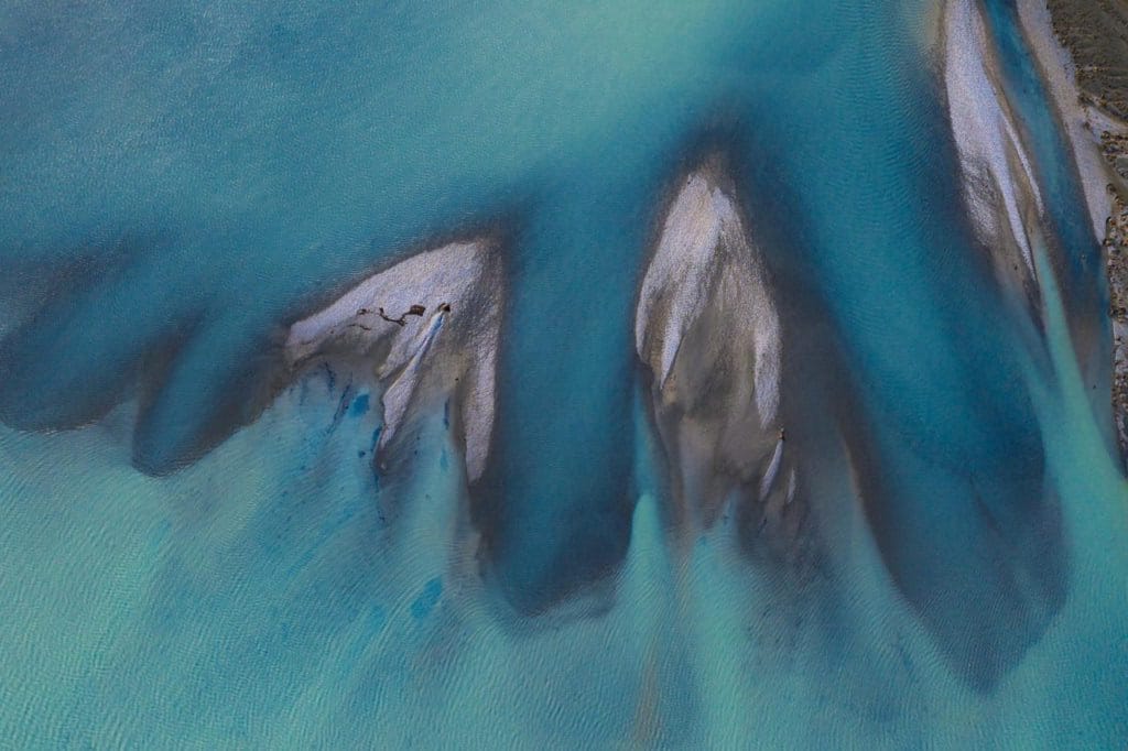Aerial view of shallow turquoise water flowing over sandbanks and creating abstract patterns.
