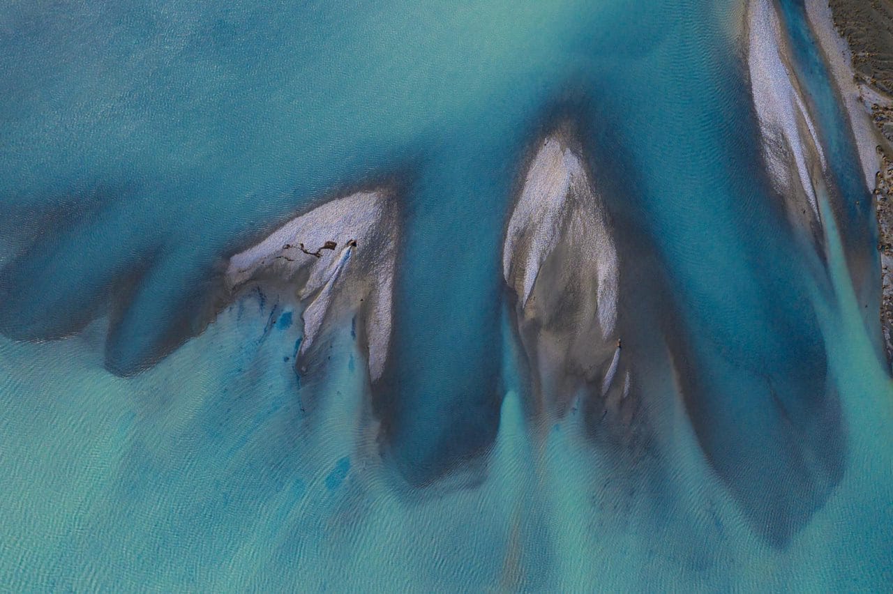 Aerial view of shallow turquoise water flowing over sandbanks and creating abstract patterns.