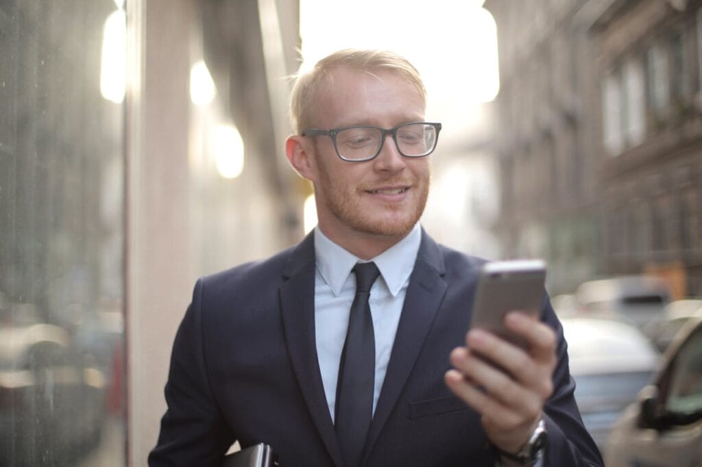 Businessman in a suit and tie smiling while looking at a smartphone, standing on a city street.
