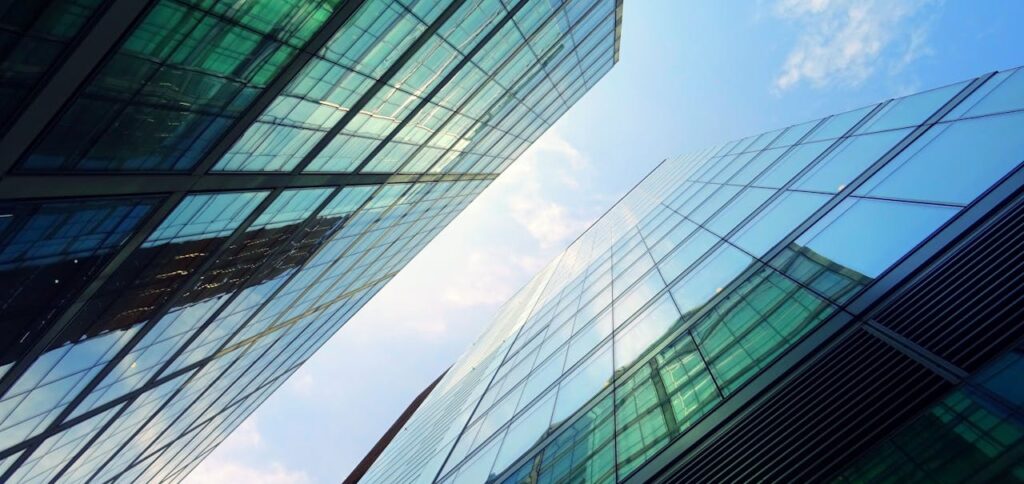 Low-angle view of two glass skyscrapers reflecting green light and the blue sky with scattered clouds.